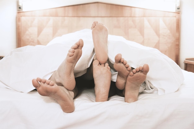 Three pairs of feet lying together under bed cover