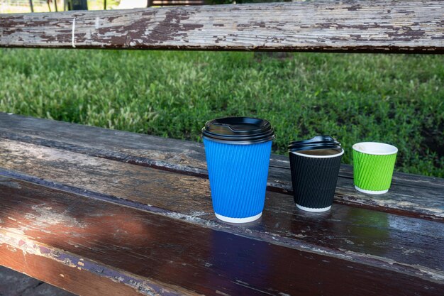 Three paper coffee cups with lids stand in a row on a wooden bench Blue black green color glasses