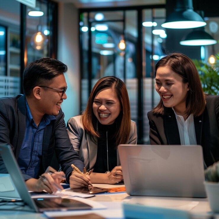 three people are sitting at a table with a laptop and a laptop