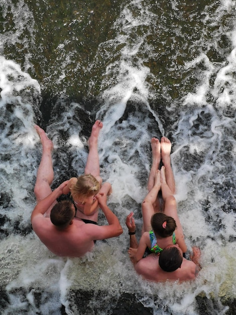 Three people are sitting in the water, one of which is wearing a green bikini.