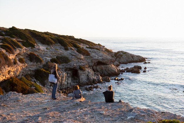 Three people a family sitting watching the sun set over the ocean