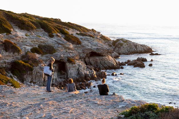 Three people a family sitting watching the sun set over the ocean