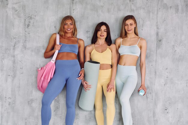 Three people standing against grey background Beautiful women in sportive clothes is indoors in the studio