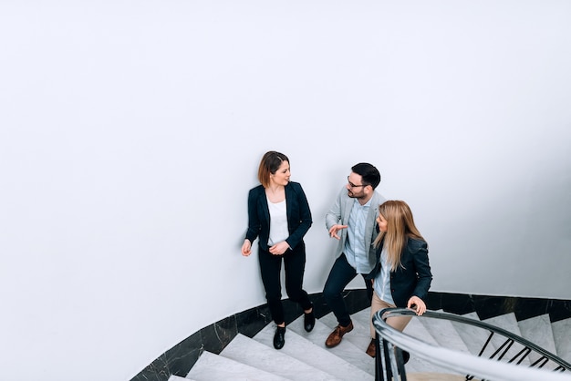 Three people talking while walking up the stairs in the office building.