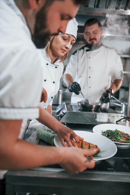 Foto tre persone che indossano insieme chef professionista che prepara il cibo in cucina