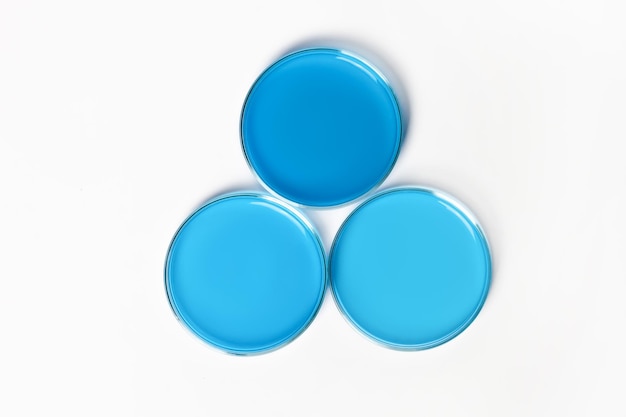 Photo three petri dishes with blue blue liquid on a white light background view from above