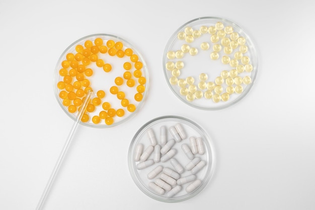흰색 격리된 배경에 주황색 노란색 및 흰색 알약 캡슐이 있는 세 개의 페트리 접시 실험실 기구 식이 보조제 및 과학적 연구 개념