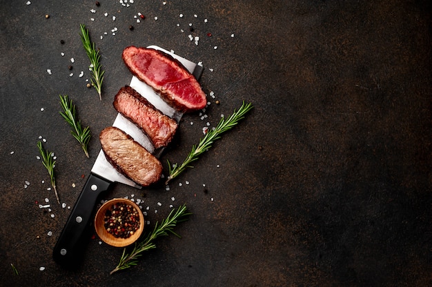 Three pieces of meat grilled over a meat knife Three types of frying meat, rare, medium, well done, with spices on stone background  with copy space for your text