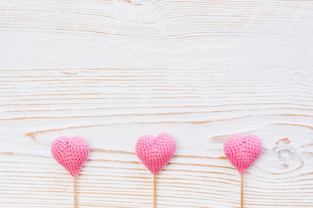 Three pink knitted hearts on sticks on a white wooden 