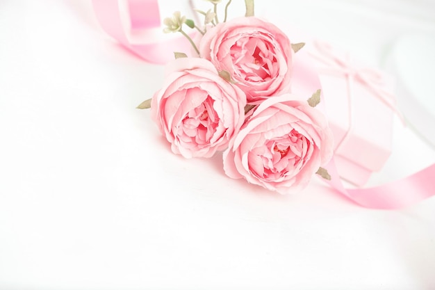 흰색 테이블에 리본과 선물 상자가 있는 분홍 장미 세 개