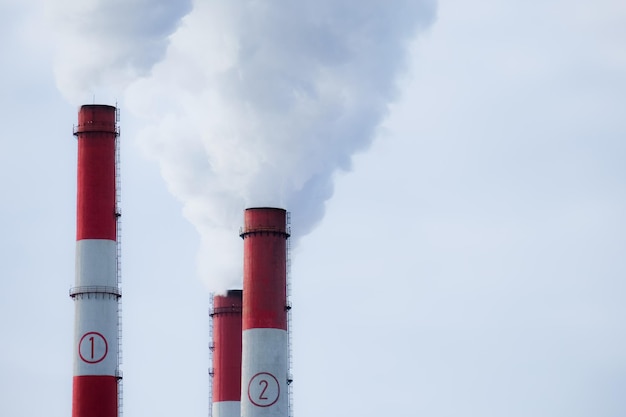 Three pipes of a thermal power plant closeup the smoke from the chimneys rises into the sky