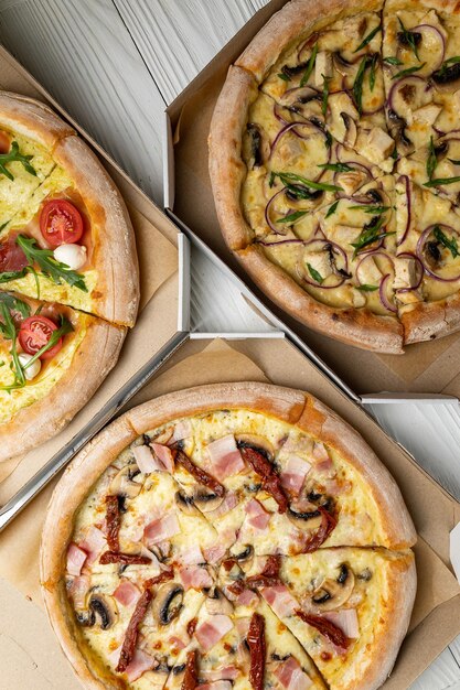 Three pizzas on a table, one with a slice of pizza on it.