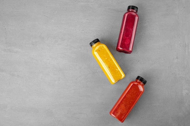 Three plastic bottles with freshly squeezed juice on gray