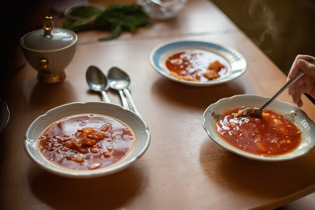 テーブルの上にボルシチが付いている3つのプレート。家族で昼食。白い皿の最初の料理。