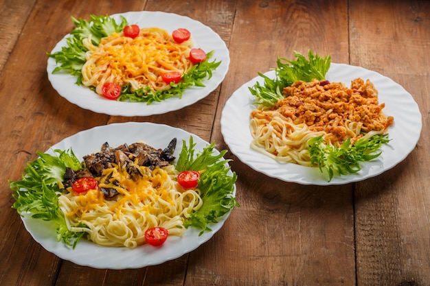 Three plates with different pasta on a wooden table decorated with herbs. Horizontal photo.