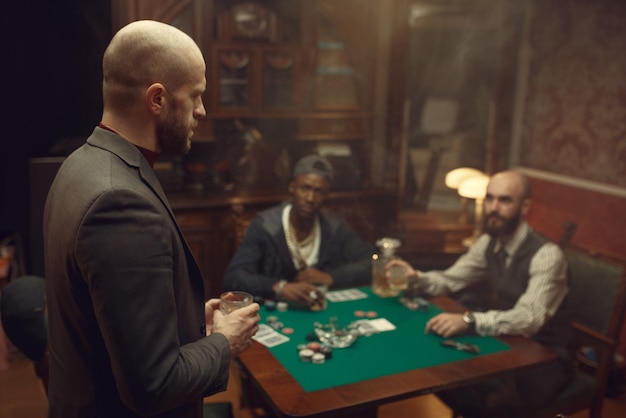 Three poker players with whiskey and cigars sitting at the table