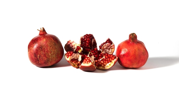 Three pomegranate fruits are depicted on a white background one of which is broken into pieces