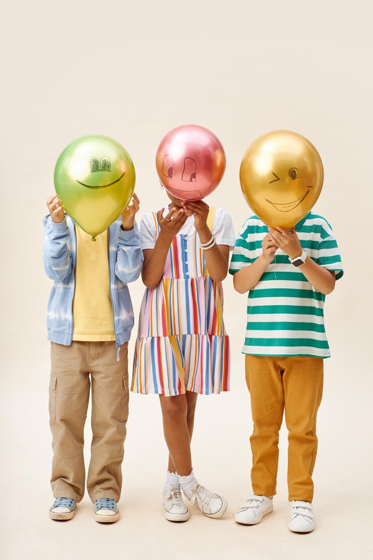 Photo three preteen kids in colorful clothes holding balloons with funny faces in studio