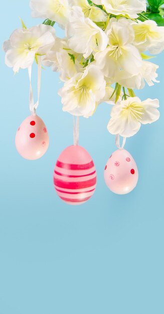 Three pretty pink Easter eggs dangling from a flowering branch against a dreamy blue sky