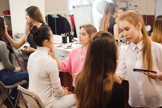 Three professional make-up artists work with beautiful young women. School of professional make-up.