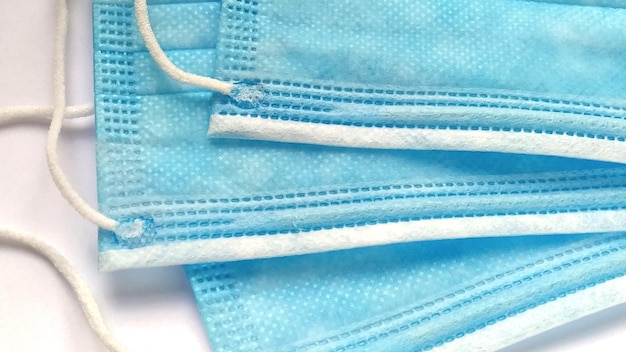 Three protective surgical masks of blue color for the face Remedy for coronavirus and bacterial infectious pathogens Synthetic material Closeup Daytime soft light White delicate background