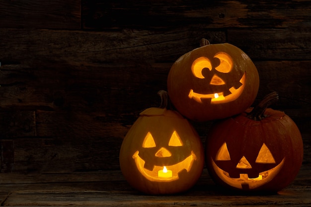 Three pumpkin jackolantern with happy faces carved halloween pumpkins with burning candles inside ha...