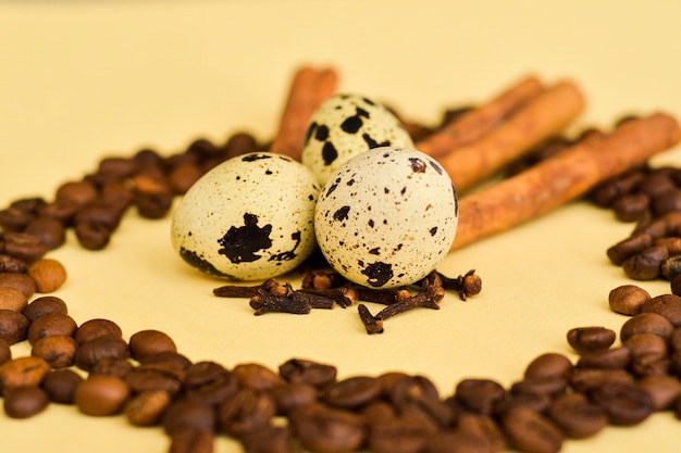 Three quail eggs and a sticks of cinnamon in the middle of the circle of coffee beans on yellow