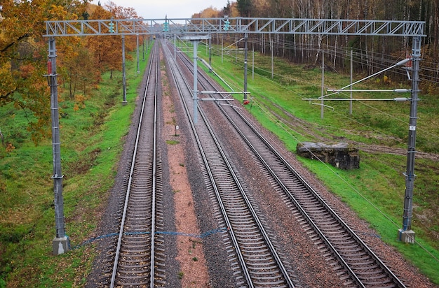 Three railway tracks in autumn time. In the frame sleepers, rubble, stones, poles, yellow and orange trees