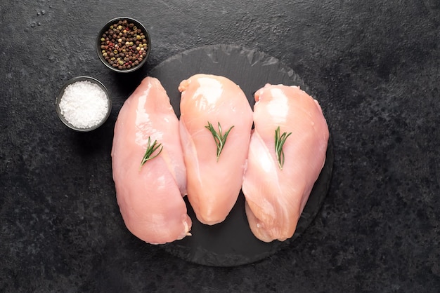 Three raw chicken breasts on stone background