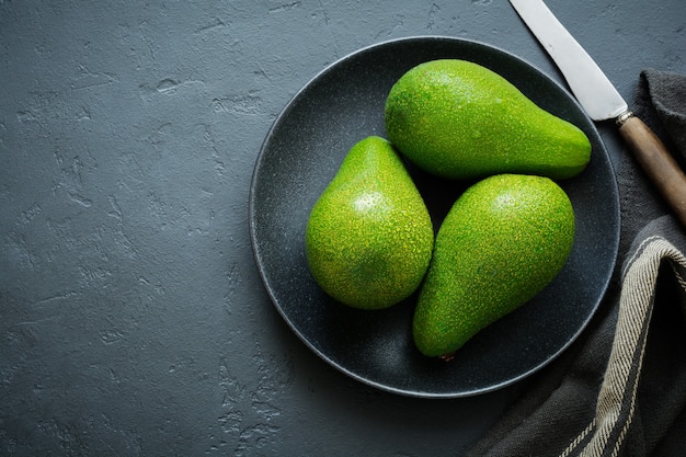 Three raw fresh avocados in black ceramic plate