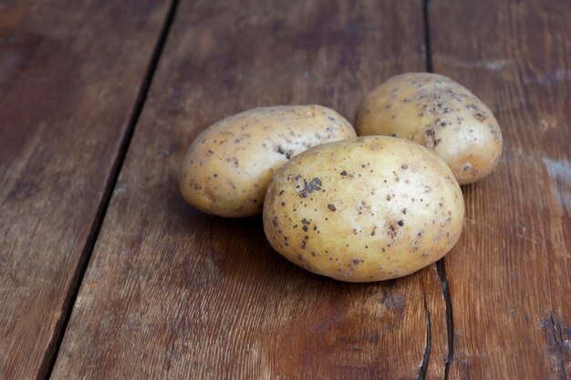 Three raw potatoes lay on vintage wooden tabletop