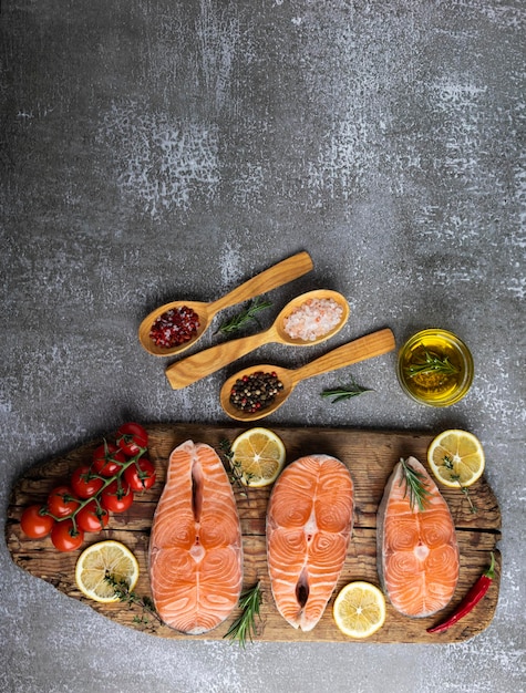 Foto tre bistecche di pesce crudo trota salmone e spezie su tavola di legno sullo sfondo scuro