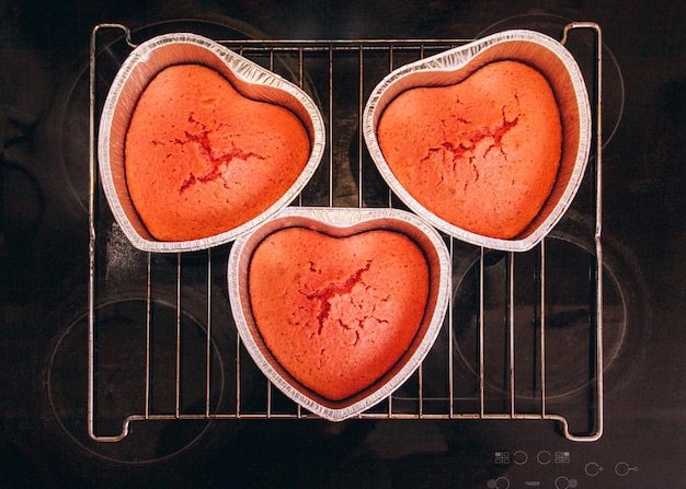 Three red cakes in heart shaped cake pan are on the hob at home