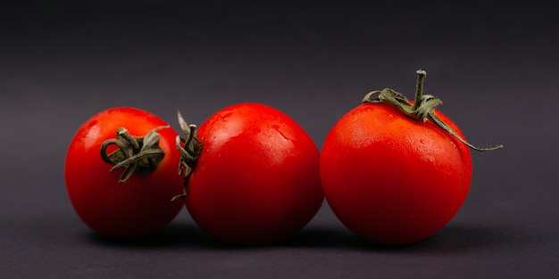 Фото Три красные сочные свежие помидоры черри на темном фоне крупным планом.