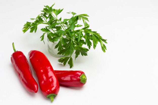 Three red peppers and parsley sprigs. White background. Copy space. Top view