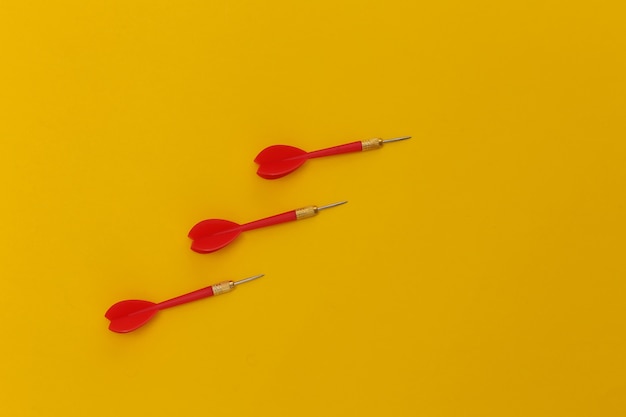 Three red plastic darts with metal tip on yellow background.