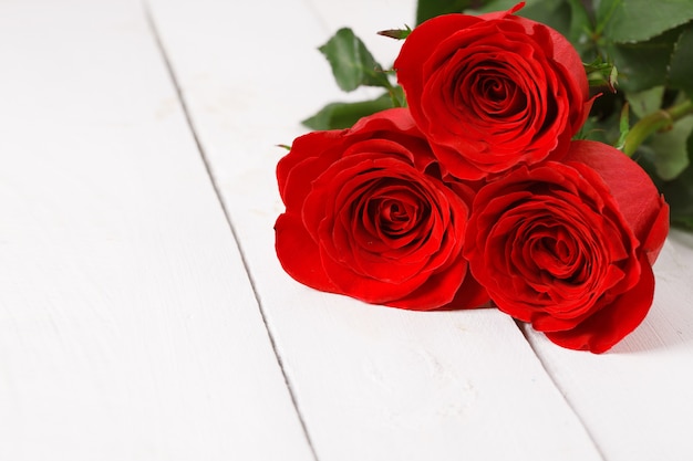 Three red roses lie on white wooden table. 