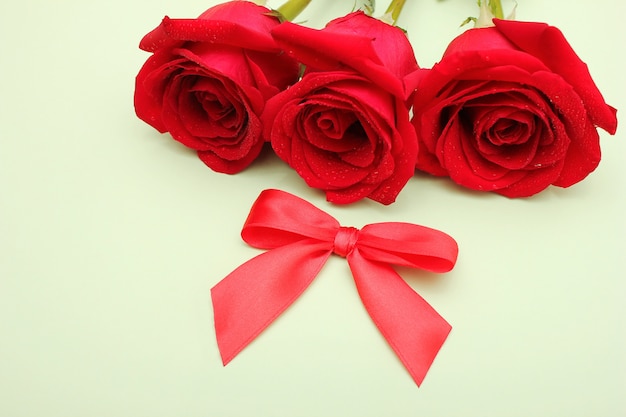 Three red roses with water drops on them and a red bow