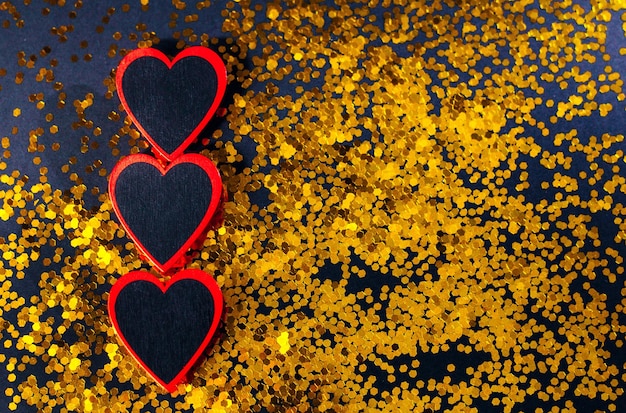 Three redblack hearts lie on a black background with gold sequins
