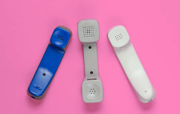 Three retro telephone handsets on pink background. Top view