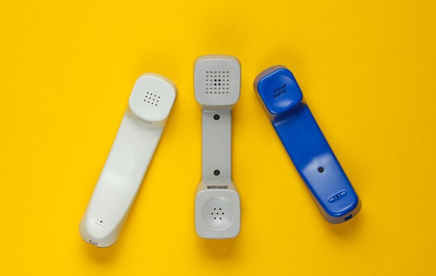 Three retro telephone handsets on yellow