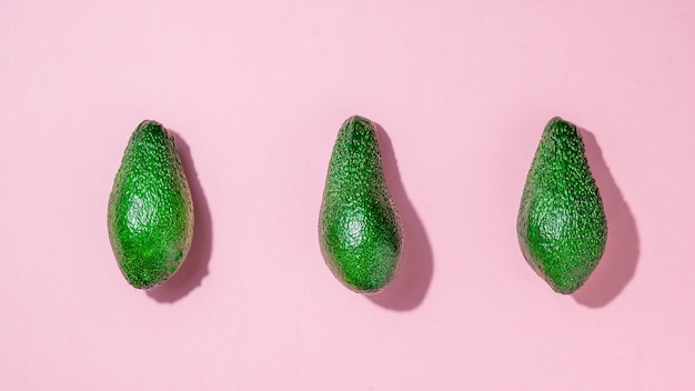 Three ripe avocados on a pink background. Delicious tropical vegetable. Flat lay.