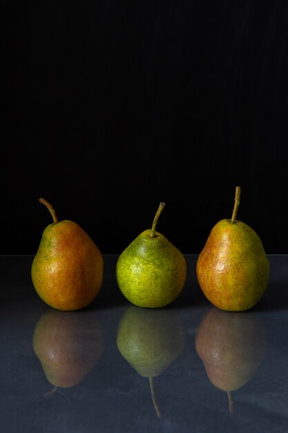 Three ripe pears are reflected in the table