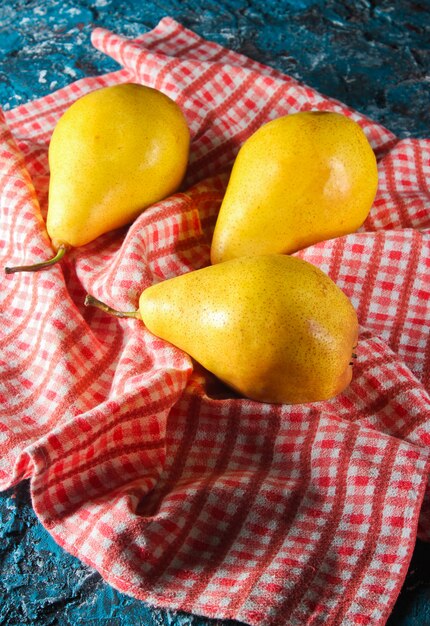 Three ripe pears on tablecloth on the blue concrete. Top view.