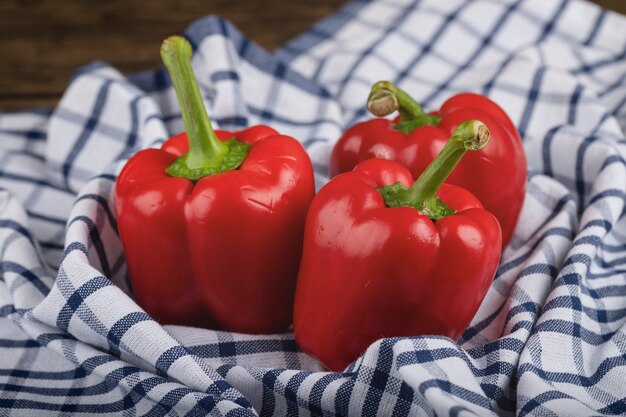 Three ripe red bell peppers with tablecloth on wooden surface