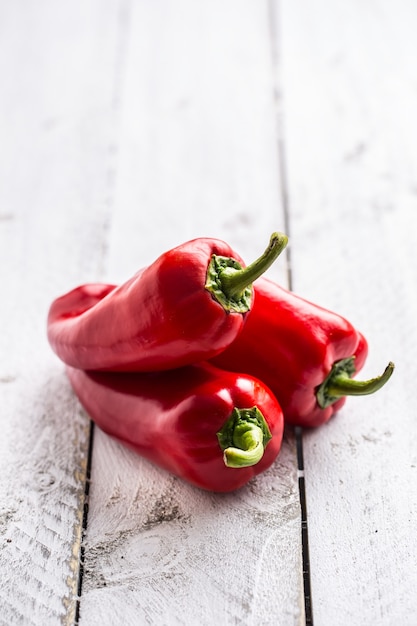 Three ripe red peppers paprika on wooden board.