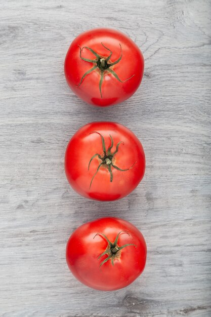 Three ripe red tomatoes placed on the grey wooden table