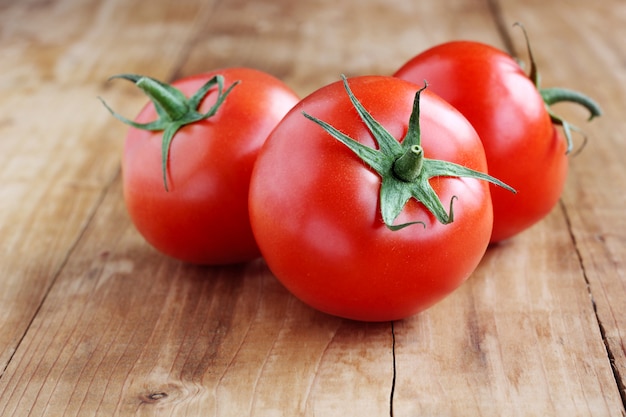 Three ripe tomato with leaves on wooden table.