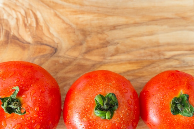 Three ripe tomatoes with water dew drops on wood