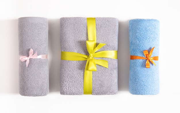 Foto tre asciugamani di spugna arrotolati e piegati legati da nastro rosa, arancione e giallo isolato. asciugamani di spugna blu e grigi contro uno sfondo bianco. vista dall'alto.
